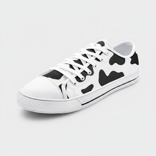 Freaky Shoes® low-top canvas sneakers featuring a black and white cow print pattern with white laces and rubber toe cap.